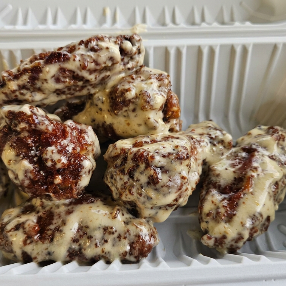 Grilled chicken wings coated in creamy sauce served in an open compostable takeout container.