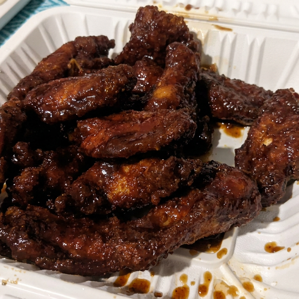 Glazed fried chicken wings piled in a white takeout container on a blue patterned tablecloth.